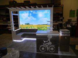 Custom Exhibit with Pergola, Product Shelves, Benches, LED Lightbox, Perimeter Accent Lights, and Counter with Storage and Standoff Graphic